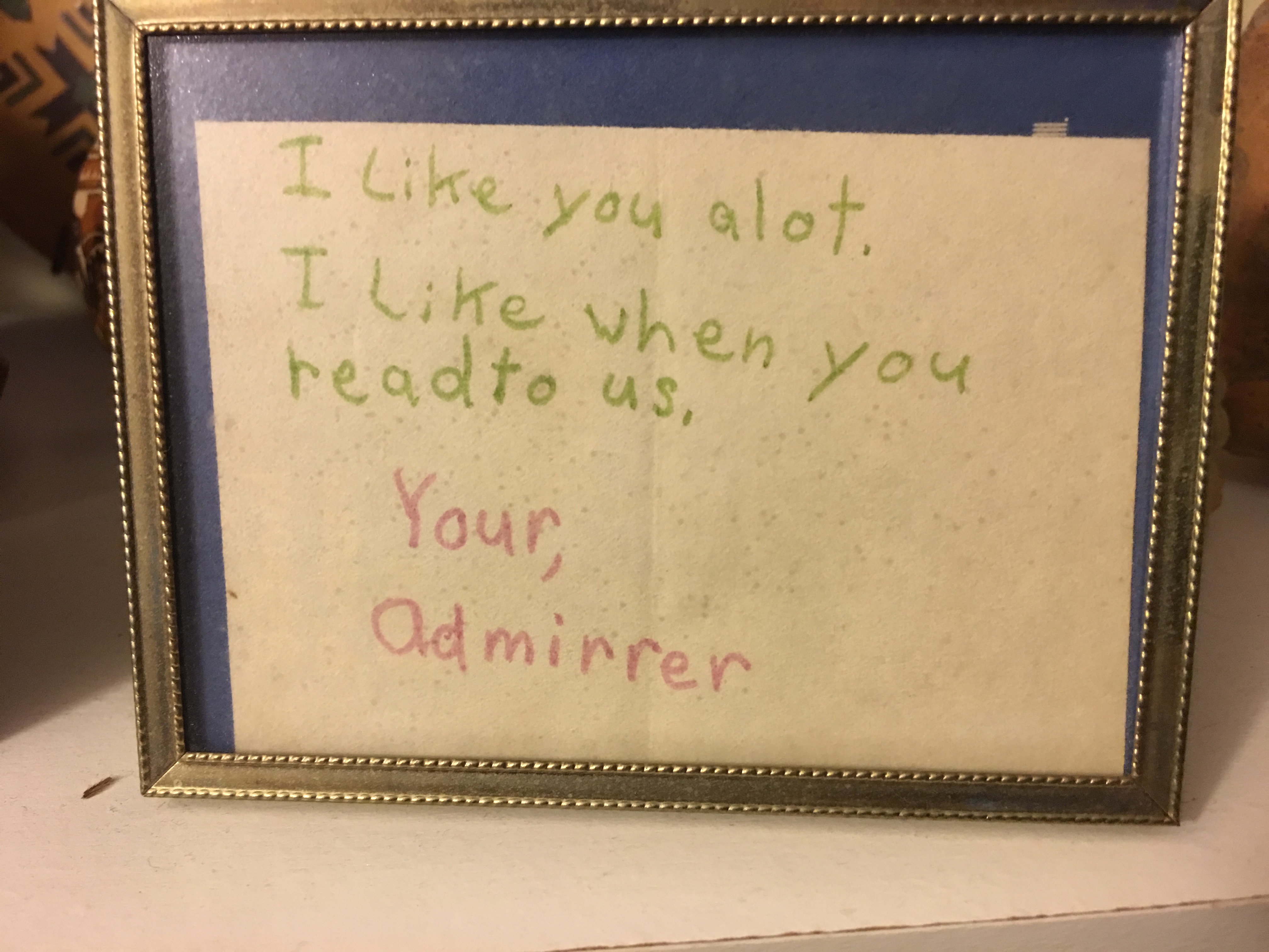Framed note from a student, stating 'I like you alot. I like when you read to us.'.